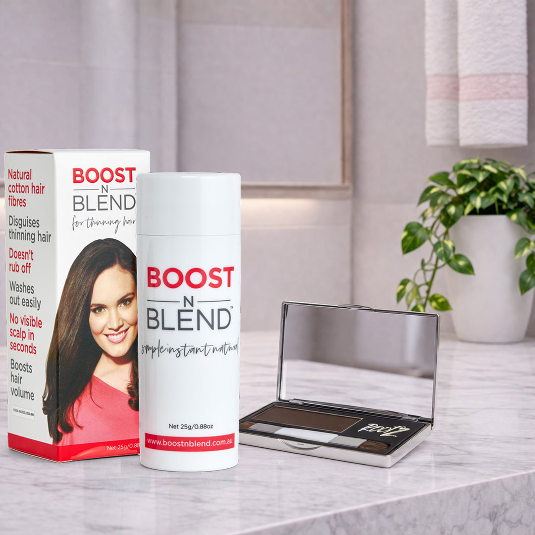 Boost N Blend hair fibers and Rootz hair concealer on a marble surface with a plant in the background