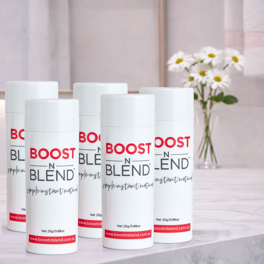 Five bottles of Boost N Blend hair fibers on a surface with a blurred background