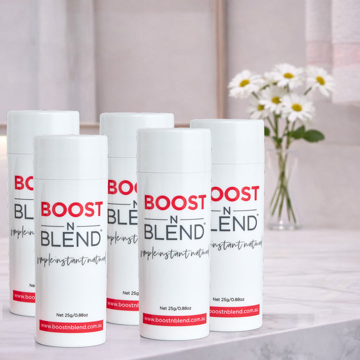 Five bottles of Boost N Blend hair fibers on a surface with a blurred background